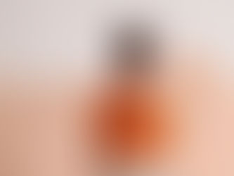 Woman in orange shirt painting a wall peach with a roller, standing in a brightly lit room.