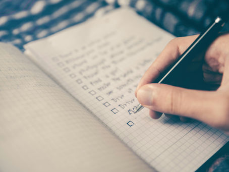 Hand writing a checklist with black pen in a grid notebook.